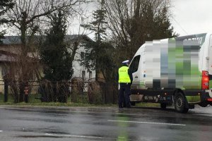 Zdjęcie przedstawia umundurowanego policjanta ruchu drogowego kontrolującego auto dostawcze