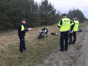 Zdjęcie przedstawia policjantów prowadzących oględziny motocykla biorącego udział w wypadku.