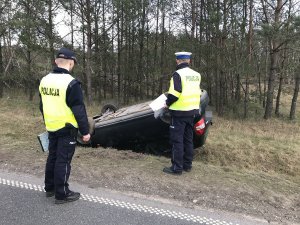 Zdjęcie przedstawia policjantów ruchu drogowego prowadzących oględziny auta biorącego udział w wypadku.