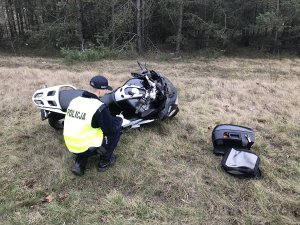 Zdjęcie przedstawia policjanta ruchu drogowego prowadzącego oględziny motocykla biorącego udział w wypadku.