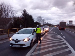 Zdjęcie przedstawia umundurowaną policjantkę ruchu drogowego prowadzącą kontrolę stanu trzeźwości kierowców