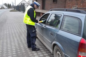 Zdjęcie przedstawia umundurowanego policjanta ruchu drogowego prowadzącego kontrolę stanu trzeźwości kierowców