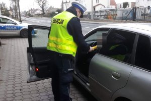 Zdjęcie przedstawia umundurowanego policjanta ruchu drogowego prowadzącego kontrolę stanu trzeźwości kierowców