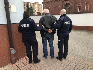 Zdjęcie przedstawia zatrzymanego prowadzonego przez umundurowanych policjantów