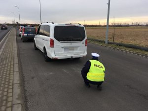 Zdjęcie przedstawia umundurowanego policjanta ruchu drogowego kontrolującego stan techniczny busa