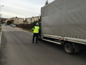 Zdjęcie przedstawia umundurowanego policjanta ruchu drogowego kontrolującego auto dostawcze