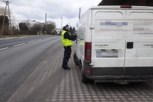 Zdjęcie przedstawia umundurowanego policjanta ruchu drogowego kontrolującego busa