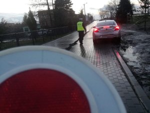 Zdjęcie przedstawia umundurowanego policjanta ruchu drogowego prowadzącego kontrolę auta osobowego