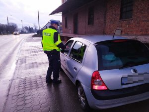 Zdjęcie przedstawia umundurowanego policjanta ruchu drogowego prowadzącego kontrolę auta osobowego