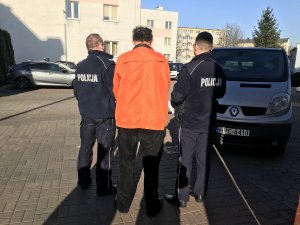 Zdjęcie przedstawia zatrzymanego podejrzanego prowadzonego przez policjantów