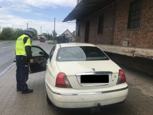 Zdjęcie przedstawia policjanta ruchu drogowego kontrolującego auto osobowe