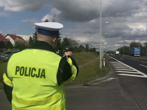 Zdjęcie przedstawia policjanta ruchu drogowego prowadzącego pomiar prędkości