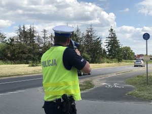 Zdjęcie przedstawia policjanta ruchu drogowego mierzącego prędkość przemieszczających się aut