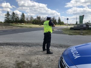 Zdjęcie przedstawia policjanta ruchu drogowego mierzącego prędkość przemieszczających się aut