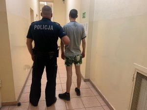 Zdjęcie przedstawia zatrzymanego prowadzonego przez umundurowanego policjanta