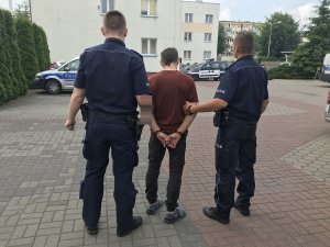 zdjęcie przedstawia zatrzymanego prowadzonego przez umundurowanych policjantów