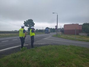 zdjęcie przedstawia policjantów ruchu drogowego, z których jeden mierzy prędkość nadjeżdżających aut.