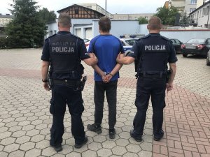 zdjęcie przedstawia zatrzymanego podejrzanego prowadzonego przez umundurowanych policjantów