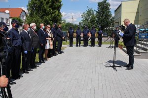 Zdjęcie przedstawia przemawiającego gościa w tle osoby uczestnicące w uroczystości