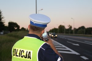 zdjęcie przedstawia policjanta ruchu drogowego kontrolującego prędkość przejeżdżających trasą aut