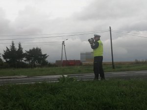 zdjęcie przedstawia policjanta mierzącego prędkość przemieszczających się aut