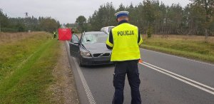 policjant stoi przed rozbitym autem uczestniczącym w wypadku