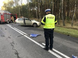 na pierwszym planie policjant. w tle rozbite auto osobowe