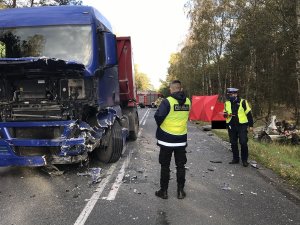 dwóch policjantów na miejscu zdarzenia, po lewej stronie rozbite auto ciężarowe