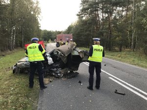 na pierwszym planie policjanci. przed nimi rozbite auto osobowe