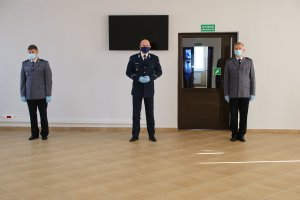 Komendant Wojewódzki Policji stoi w sali wspólnie ze zdającym obowiązki i przejmującym je
