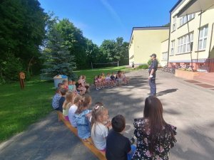 policjant uczy siedzące na ławkach dzieci przepisów drogowych