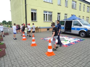 dzieci idą po torze przeszkód w goglach, obok idzie policjantka