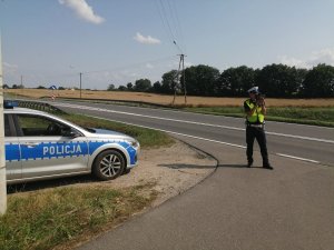 policjant kontroluje prędkość urządzeniem. po lewej stronie zdjęcia radiowóz