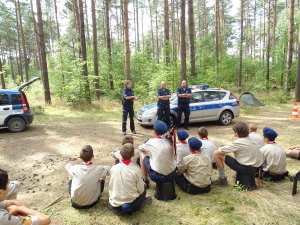 policjanci stoją przy radiowozie i opowiadają o swojej pracy, skauci siedzą na  trawie