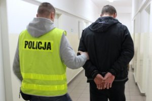 policjant ubrany w żółtą kamizelkę prowadzi zatrzymanego. zdjęcie ilustracyjne