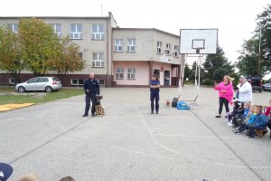 przewodnik opowiada o swojej pracy. przy nodze siedzi mu pies, obok stoi policjantka