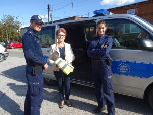 kobieta, która otrzymała kamizelkę odblaskową pozuje do zdjęcia razem z policjantami