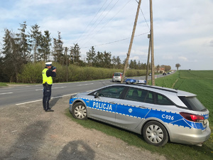 na pierwszym planie radiowóz. w tle policjant mierzy prędkość