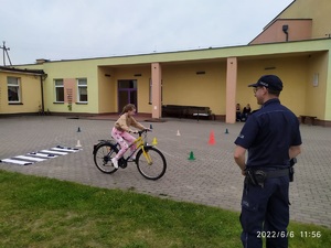 dziewczynka pokonuje tor przeszkód rowerem nadzorowana przez policjanta