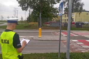 policjant przy przejściu dla pieszych wypełnia dokumentację z prowadzonej kontroli okolic szkół