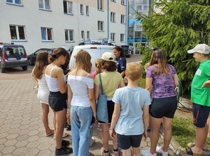 Policjanci prowadzący pogadankę z dziećmi  w ramach ,,Bezpiecznych wakacji&quot; na terenie KPP Nakło.