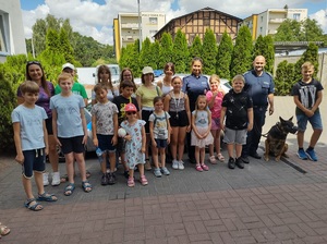 Policjanci prowadzący pogadankę z dziećmi  w ramach ,,Bezpiecznych wakacji&amp;quot; na terenie KPP Nakło.